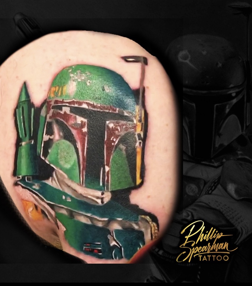 This iconic Boba Fett piece anchors the start of a Star Wars half sleeve, capturing the weathered patina of his helmet and armor. The distinct greens, deep reds, and scuffed metallic accents are rendered with a precise texture that brings this legendary bounty hunter to life on the skin.