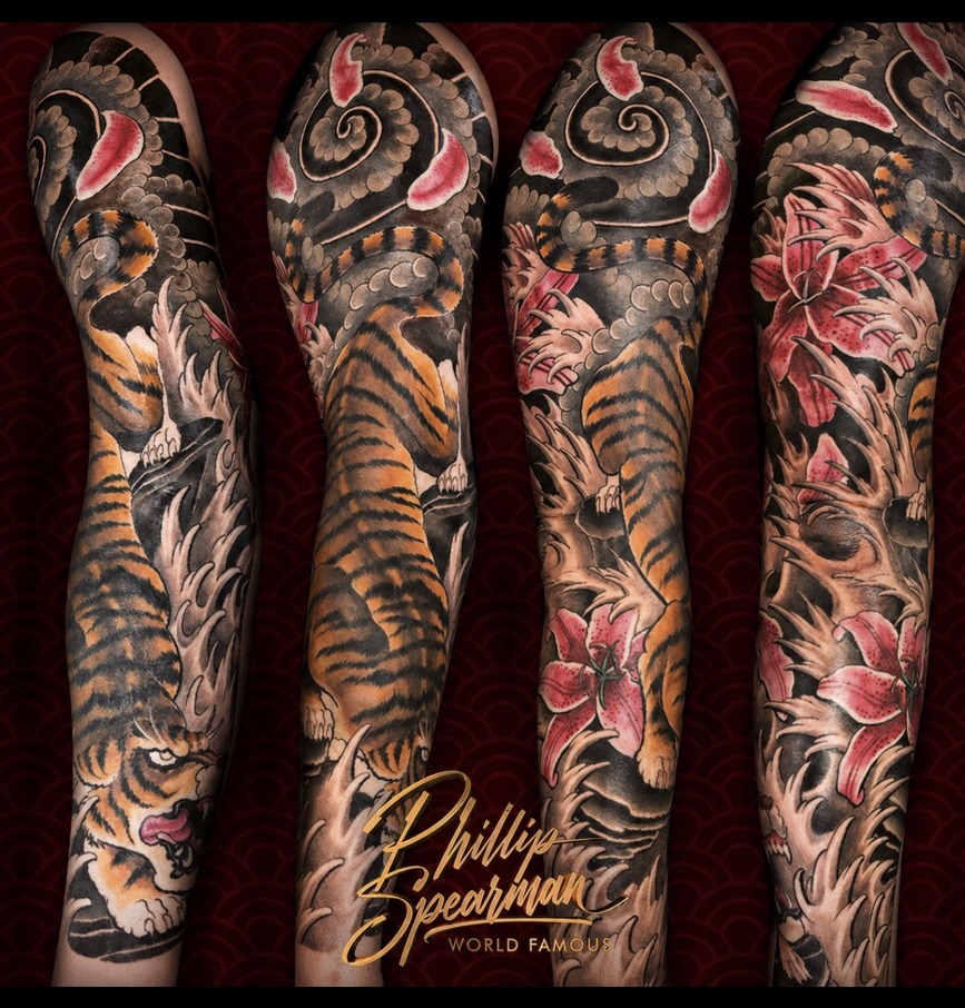 This magnificent Japanese tiger and lily flower sleeve is a true cover-up, meticulously designed freehand to rebuild the arm's surface. The vibrant tiger stripes and crimson lilies beautifully wrap the muscle lines, ensuring the previous tattoo is entirely concealed, with nothing of the old work visible beneath.